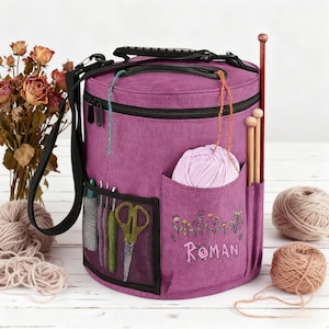 May include: A purple yarn storage bag with multiple pockets, a handle, and a shoulder strap. The bag has a pocket with a ball of light purple yarn, and another with scissors and knitting needles. The word "ROMAN" is embroidered on the front.
