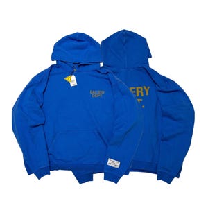 May include: Two blue hoodies with front and back views. The front of the hoodie on the left has the text "GALLERY DEPT." in gold. The back of the hoodie on the right has the text "GALLERY" in gold. Both hoodies have a front pocket and a hood.