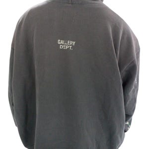 May include: Dark gray hoodie with the text "GALLERY DEPT." printed in white on the back. The hoodie has a hood and long sleeves. The fabric appears to be a soft, comfortable material.