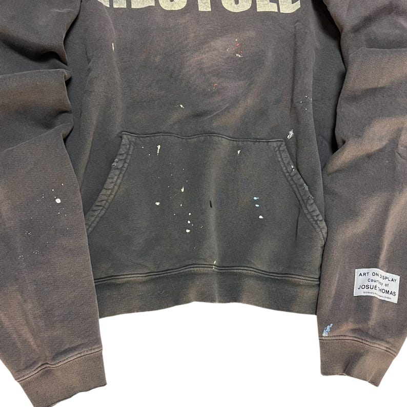 May include: Dark gray hoodie with white paint splatters and the word "RECYCLED" across the chest. Features a front pocket and a small tag on the sleeve that reads "ART ON DISPLAY Country of JOSUE THOMAS."
