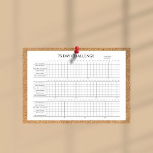Puede incluir: Un rastreador blanco de 75 Day Challenge sujeto a un corcho con un imperdible rojo. El rastreador incluye espacios para tareas diarias y una cuadr&iacute;cula para marcar el progreso. El texto "75 DAY CHALLENGE" est&aacute; en la parte superior.