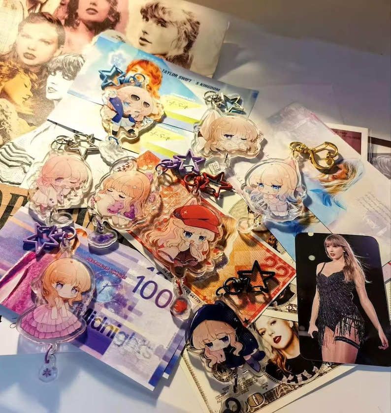 May include: A collection of acrylic keychains featuring anime-style illustrations of a blonde character in various outfits. The keychains are scattered on a surface with images of a singer and currency.