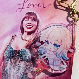 May include: A pink and purple Lover-themed print featuring a photo of a woman and the word "Lover" in glittery script. A clear acrylic charm with a cartoon character and gold-colored heart-shaped clasp is attached.