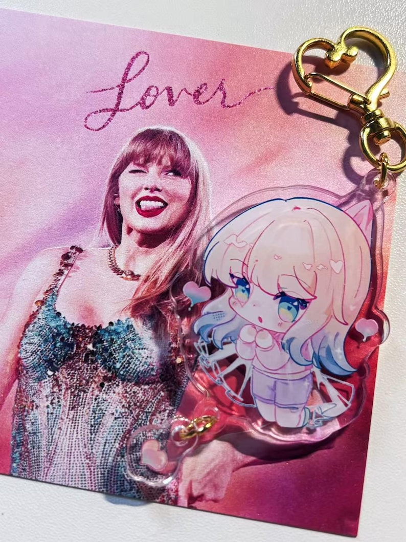 May include: A pink and purple Lover-themed print featuring a photo of a woman and the word "Lover" in glittery script. A clear acrylic charm with a cartoon character and gold-colored heart-shaped clasp is attached.