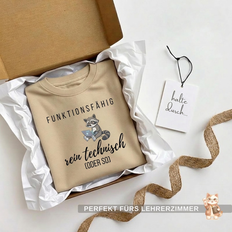 May include: A tan sweatshirt with the words "FUNKTIONSF&Auml;HIG rein technisch (ODER SO)" and a raccoon graphic. The sweatshirt is in a cardboard box with white tissue paper. A tag with "halte durch..." is attached.