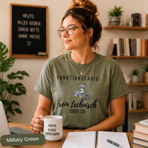 May include: Military green t-shirt with the text "FUNKTIONSF&Auml;HIG" and a raccoon graphic using a laptop. The shirt also has the text "rein technisch (ODER SO)". A white mug with the text "KAFFEE. KLASSE. KATASTROPHE" is visible.