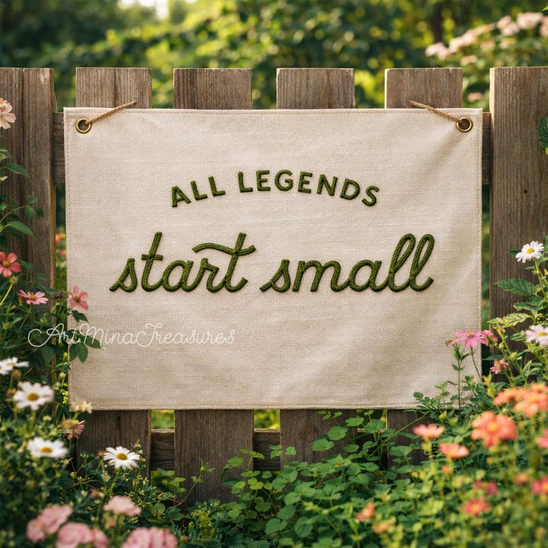 Puede incluir: Una pancarta de lona beige con el texto "ALL LEGENDS start small" en verde, colgada de una valla de madera. La pancarta est&aacute; enmarcada por un exuberante jard&iacute;n con flores coloridas y vegetaci&oacute;n, creando una escena natural y acogedora.