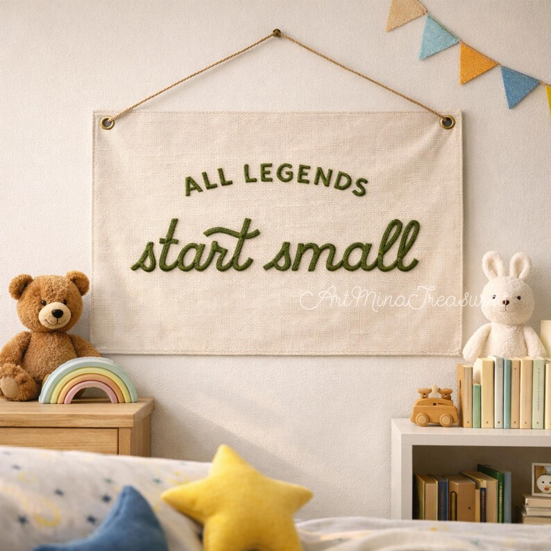 Puede incluir: Un tapiz de pared de tela beige con el texto "ALL LEGENDS start small" en escritura verde. El letrero est&aacute; suspendido por una cuerda. Un oso de peluche y un conejito de peluche est&aacute;n a ambos lados. Decoraci&oacute;n de habitaci&oacute;n infantil.
