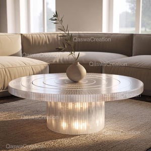 Puede incluir: Una mesa de centro redonda y blanca con una base de estilo mosaico y un diseño circular en la parte superior. Un pequeño jarrón beige con una ramita de vegetación encima. La mesa está en un salón.