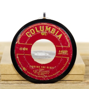 May include: A red and black 45 RPM vinyl record with a gold Columbia logo and the text "Singing the Blues" by Guy Mitchell with Ray Conniff and his orchestra. The record number is 4-40769 (ZSP 39219).