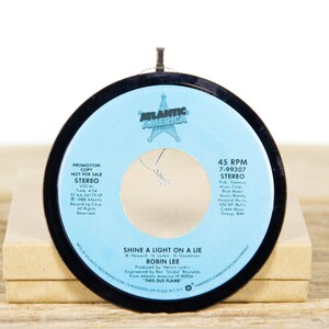 May include: A blue and black 45 RPM record with a silver star in the center. The record is titled "Shine a Light on a Lie" by Robin Lee. The record is a promotional copy and is not for sale.