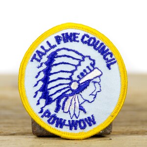 Peut inclure: Un écusson brodé bleu et jaune avec le texte "Tall Pine Council" et un motif de coiffe amérindienne.