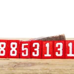 Op de afbeelding: Rode viltpleisters met witte cijfers 8853131 op een houten oppervlak.