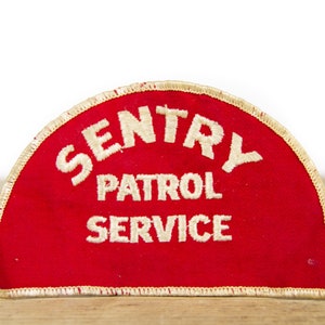 Może przedstawiać: Czerwona naszywka z tkaniny z białym haftem, na którym widnieje napis "Sentry Patrol Service".