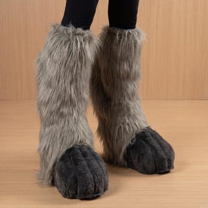 May include: Gray furry costume boots with dark gray paw-like feet. The boots extend up the legs, creating a whimsical and playful look. The faux fur is a soft, neutral gray color.