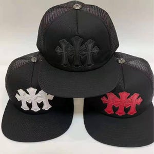 Puede incluir: Gorras de camionero negras con la parte trasera de malla y visera curva. Cada gorra presenta un diseño de cruz en la parte delantera en negro, blanco o rojo. Las gorras tienen un botón plateado en la parte superior.