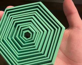 May include: A green, nested hexagonal shape, with each layer decreasing in size towards the center. The object is made of a solid material and has a textured surface. The design is geometric and modern.