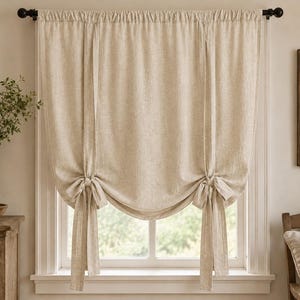 Peut inclure: Un rideau beige à nouer en tissu texturé. Le rideau est suspendu à une tringle noire et comporte deux liens verticaux en tissu noués en bas, créant un effet drapé, froncé et souple sur toute la largeur de la fenêtre.