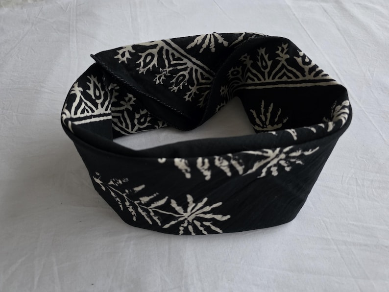 May include: Black headband with a white floral pattern. The fabric is folded over, creating a thick band. The headband is likely for fashion or to keep hair out of the face.