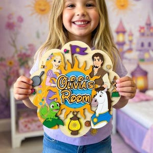 May include: A wooden sign in the shape of a flower, featuring characters from a fairy tale. The sign says "Olivia's Room" in a yellow, stylized font. The sign has a sun design and includes a purple flag.