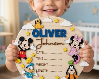 May include: A wooden, round baby announcement sign featuring the name "OLIVER Johnson" in blue and brown lettering. The sign is decorated with Disney characters Mickey Mouse, Minnie Mouse, Donald Duck, Goofy, and Pluto. Includes spaces for date, time, weight, and length.
