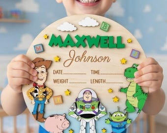 May include: A circular wooden birth announcement sign featuring Toy Story characters including Woody, Buzz Lightyear, Rex, and an alien. The sign displays the name MAXWELL Johnson in green and brown text, with blank lines for date, time, weight, and length.