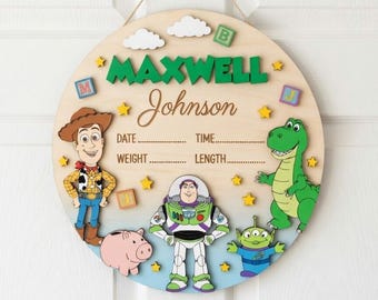 May include: A circular wooden wall sign featuring Toy Story characters including Woody, Buzz Lightyear, Rex, Hamm, and an alien. The sign displays the name Maxwell Johnson and includes blank lines for date, time, weight, and length details.
