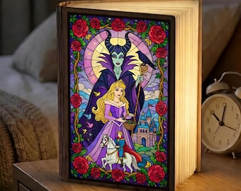 May include: A wooden book-shaped lamp with a stained glass design featuring a princess, a villain, and a castle. The artwork is framed by red roses. The pages of the book are illuminated.