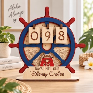 Könnte beinhalten: Ein hölzerner Countdown-Kalender in Form eines Schiffssteuerrads mit roten und blauen Akzenten. Er verfügt über drei hängende Holzplättchen mit der Zahl 098, eingravierte Wellenmuster, ein rotes Kreuzfahrtschiff-Symbol und den Text DAYS UNTIL OUR DISNEY CRUISE.
