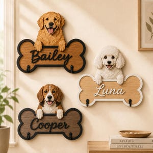May include: Three wall-mounted bone-shaped plaques featuring sculpted dog heads and two black hooks each. The plaques display the names Bailey, Luna, and Cooper in raised lettering. The dogs are a golden retriever, a white poodle, and a beagle.