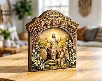 May include: A wooden plaque with an arched top, featuring a religious scene. The plaque has the words "HE IS RISEN! HALLELUJAH!" at the top. The scene depicts Jesus with open arms, an angel, and lilies. The plaque is on a wooden table.