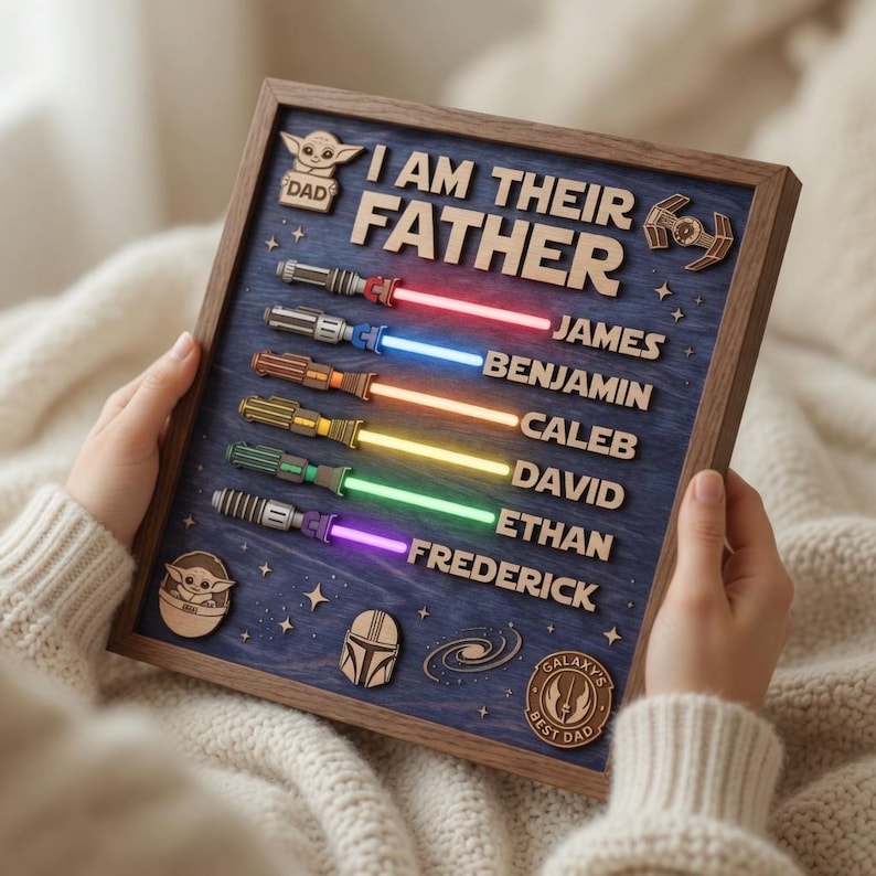 Może przedstawiać: Drewniany szyld w ramie z napisem "I AM THEIR FATHER" oraz imionami James, Benjamin, Caleb, David, Ethan i Frederick. Szyld przedstawia drewniane miecze świetlne z r&oacute;żnokolorowymi ostrzami i ikonami z motywem Gwiezdnych Wojen.