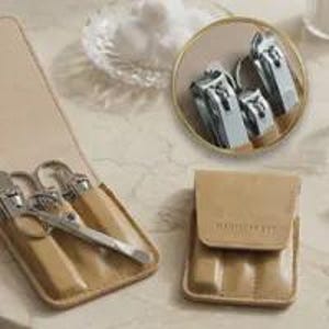 May include: A tan leather manicure kit case containing silver metal nail clippers and grooming tools. The case features a flap closure with the text MANICURE KIT embossed on the front. A circular inset shows the silver tools in greater detail.