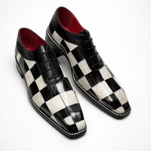 May include: A pair of black and white checkered dress shoes with black laces and a red interior. The shoes have a glossy finish and a stitched white border around the sole.