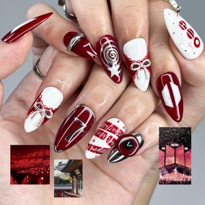 May include: A collection of long, almond-shaped nails in red and white. Some nails are decorated with silver bows, swirls, and the number 7. Other nails feature text, including the letters "RM JIN SUGA HOPE JIMIN V JUNGKOOK".