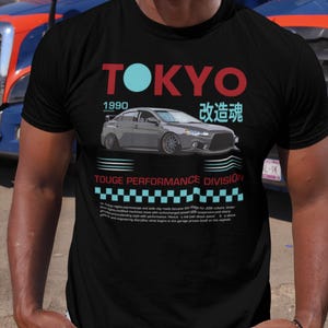 May include: Black t-shirt with a graphic design featuring the word "TOKYO" in red and a light blue circle, the year "1990", and a gray car illustration. The text "TOUGE PERFORMANCE DIVISION" is also present.