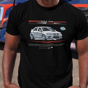 May include: Black t-shirt featuring a silver car graphic with the text "WORLD TOUR RACING" and "90s". The car design includes a front spoiler and side skirts. The shirt has a crew neck and short sleeves.