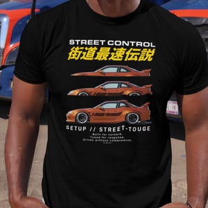 May include: Black t-shirt with orange car graphics and text. The text reads "STREET CONTROL" and "SETUP // STREET-TOUGE". The shirt also has Japanese text. The design features three stylized car illustrations.