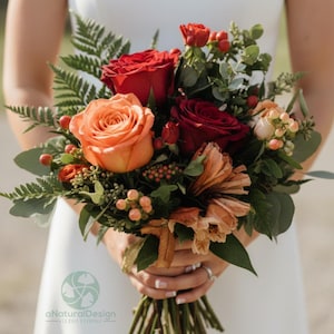May include: A vibrant bouquet featuring red and orange roses, accented with greenery and berries. The bouquet is held by a person wearing a white dress. The bouquet includes the text "aNaturalDesign STUDIO FLORIST".