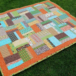 May include: A patchwork quilt with a variety of colors and patterns, including brown, green, blue, orange, and yellow. The quilt is made of squares and rectangles, and the edges are trimmed with a green fabric.