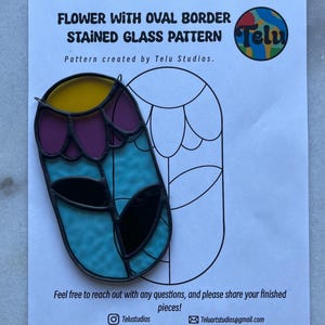 May include: A stained glass pattern for a flower with an oval border. The design features yellow, purple, turquoise, and black glass pieces. The pattern is on a white paper with the text "FLOWER WITH OVAL BORDER STAINED GLASS PATTERN" and the Telu Studios logo.