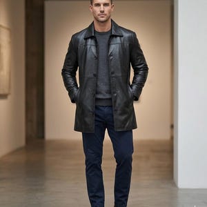 Può includere: Un cappotto in pelle nera con chiusura a bottoni, indossato sopra un maglione grigio e pantaloni blu navy. Il cappotto ha un design classico con colletto e tasche. La persona indossa stivali in pelle marrone.