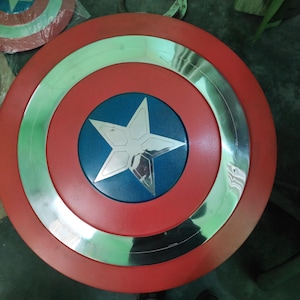 Op de afbeelding: Een rood, wit en blauw schild met een zilveren ster in het midden. Het schild heeft een cirkelvormig ontwerp met een zilveren rand. Het schild is een replica van Captain America's schild.