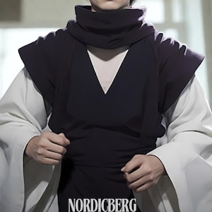 Peut inclure: Un haut noir avec un col montant et un col en V, superposé à un vêtement blanc à manches longues. Les manches sont larges et fluides. Le mot "NORDICBERG" est imprimé en bas.