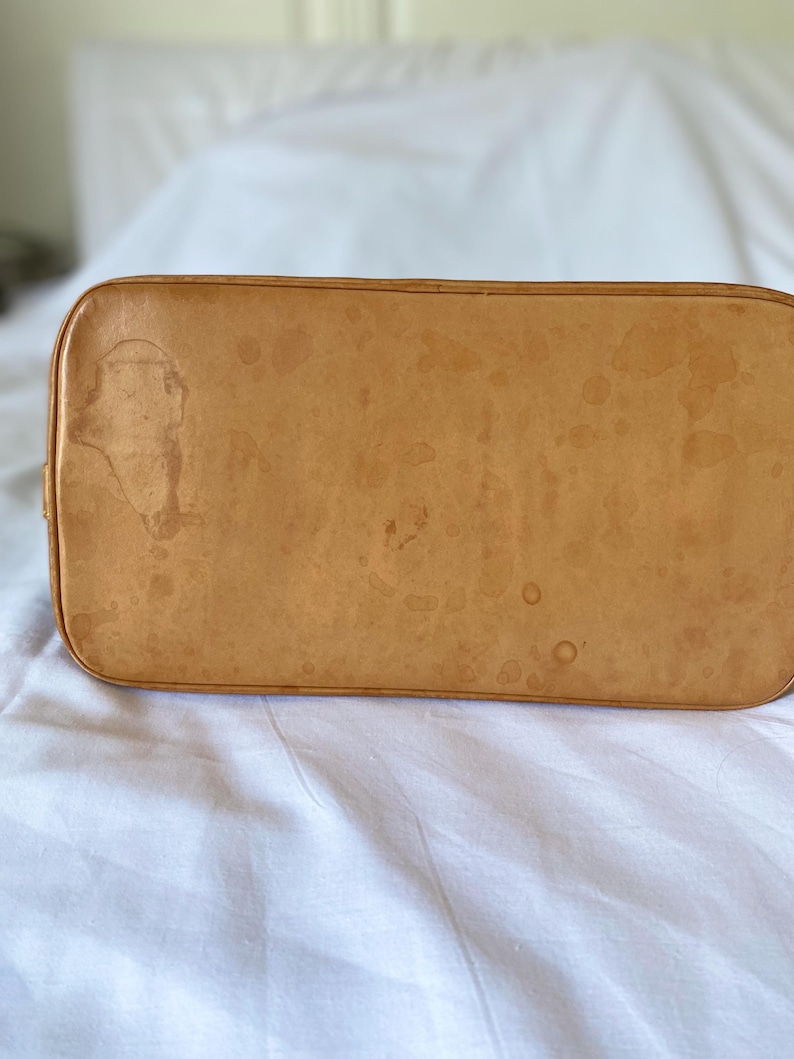 K&ouml;nnte beinhalten: Nahaufnahme des Bodens einer hellbraunen Lederhandtasche. Das Leder weist dunkelbraune Wasserflecken und -punkte auf. Die Tasche hat abgerundete Ecken und eine glatte Oberfl&auml;che.