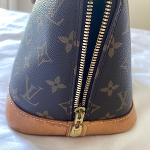 K&ouml;nnte beinhalten: Braune Handtasche mit goldenem Rei&szlig;verschluss und hellbraunem Boden. Die Tasche hat ein sich wiederholendes Muster aus braunen Blumen- und Logodesigns. Der Rei&szlig;verschluss ist ge&ouml;ffnet und gibt den Blick ins Innere frei.