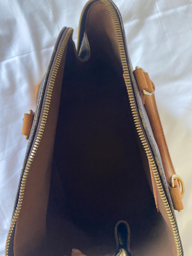 K&ouml;nnte beinhalten: Offene Ansicht einer braunen Handtasche mit goldenem Rei&szlig;verschluss und hellbraunen Lederakzenten. Der Innenraum ist dunkelbraun. Die Tasche hat eine strukturierte Form und einen oberen Griff. Die Tasche besteht aus einem gemusterten Material.
