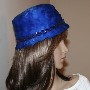 May include: A vibrant blue feather hat with a decorative beaded band. The hat is a deep cobalt blue and appears to be made of soft feathers. The beaded band adds a touch of elegance to the hat's design. The hat is a stylish accessory.