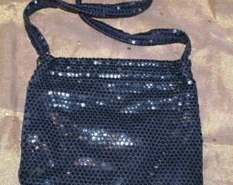 May include: A navy blue evening bag covered in small, reflective sequins. The bag has a matching strap and a rectangular shape. The sequins catch the light, creating a shimmering effect. The bag is suitable for formal events.