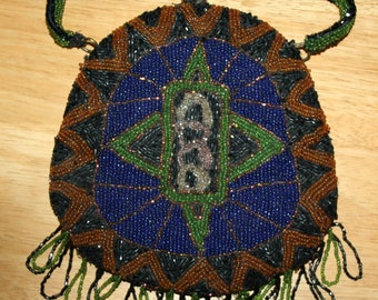 May include: A vintage beaded handbag with a clasp closure. The bag features a geometric design in blue, brown, black, and green beads. A green beaded handle and fringe complete the design. The bag is likely from the early 20th century.